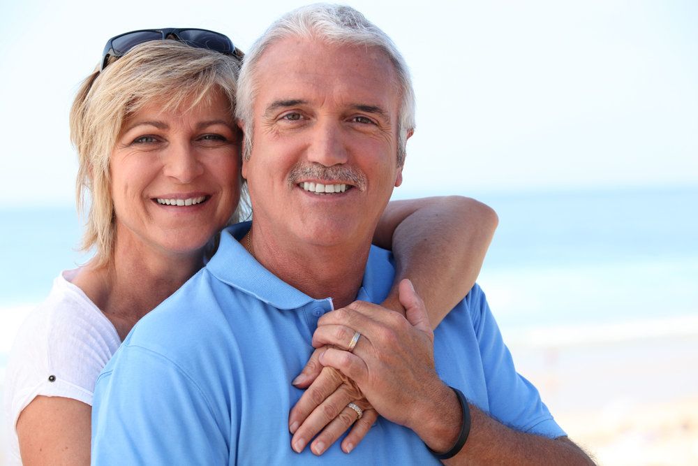 A handsome smiling couple hold one another in a warm embrace.